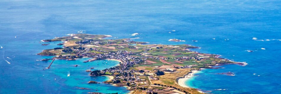 Vue aérienne de l'île d'Ouessant, au large du Finistère, montrant le bourg de Lampaul, son port, ses paysages côtiers et les eaux turquoise de la mer d'Iroise.